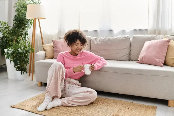 A young woman enjoys a warm drink while relaxing on a plush sofa. — Stock Photo