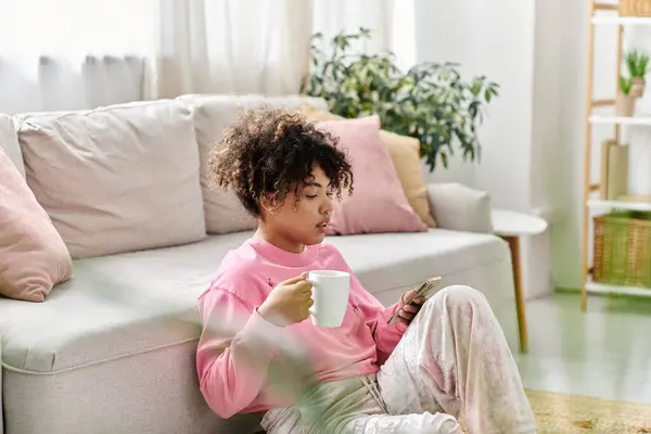 Uma jovem mulher desfruta de uma bebida quente e percorre seu telefone em um ambiente sereno. — Fotografia de Stock