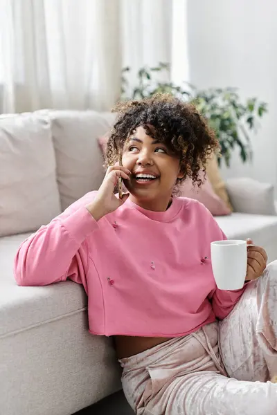 A cheerful woman relaxes on the couch, sipping tea and chatting on the phone. — Stock Photo