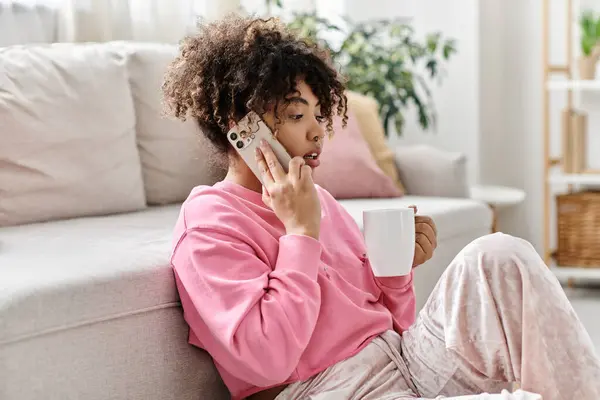 Una giovane donna si rilassa a casa mentre parla al telefono e beve caffè. — Foto stock