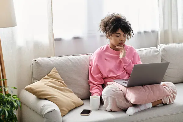 A young woman relaxes on her couch, focusing intently on her laptop. — Stock Photo