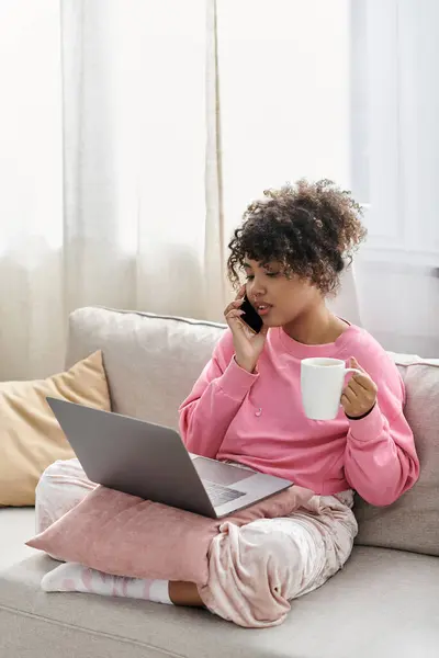 A young woman chats on the phone while sipping a drink at home. — Stock Photo
