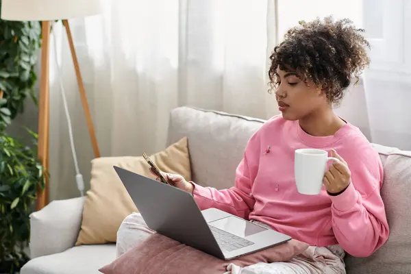 A young woman relaxes at home, sipping coffee and focused on her laptop. — Stock Photo