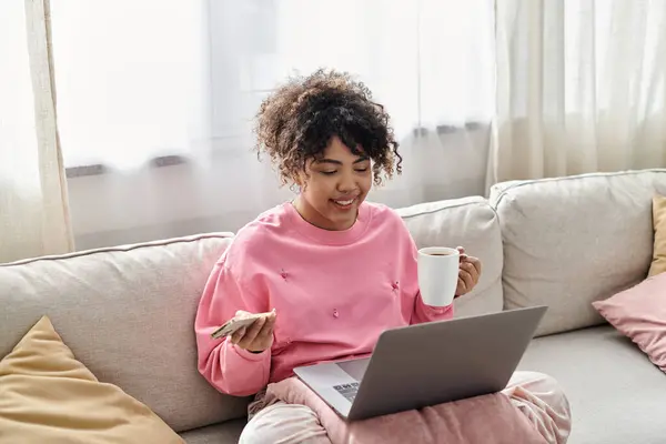 Smiling woman relaxes on the couch with a laptop and a warm drink. — Stock Photo