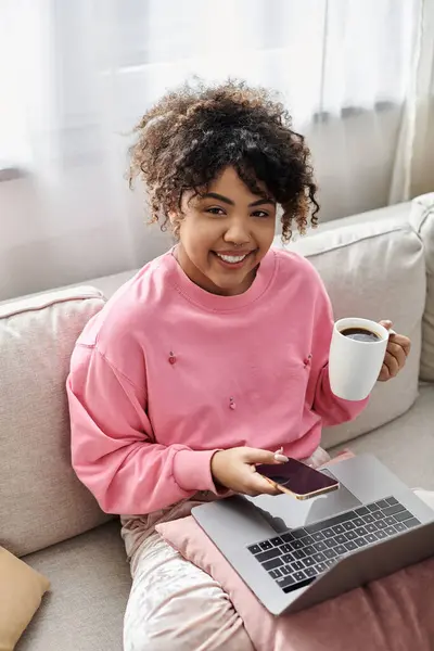 A joyful young woman sips coffee while using her laptop at home. — Stock Photo