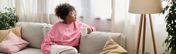 A woman sips tea, lost in thought, amidst cozy home surroundings. — Stock Photo