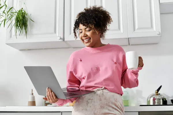 Donna allegra si rilassa a casa mentre lavora sul suo computer portatile con una tazza di caffè. — Foto stock