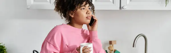 Talking on the phone, she sips coffee in her serene kitchen. — Stock Photo