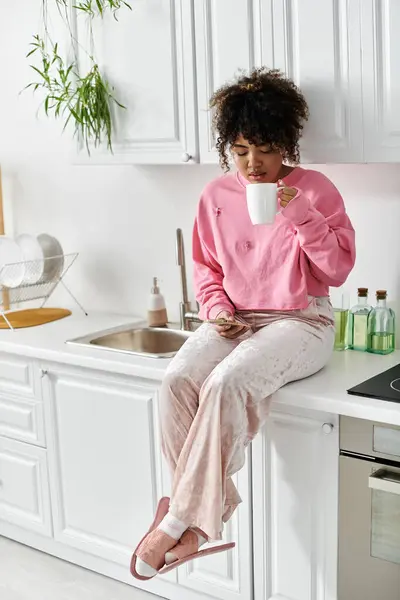 A woman sits casually on the countertop sipping her drink and reading a book. — Stock Photo