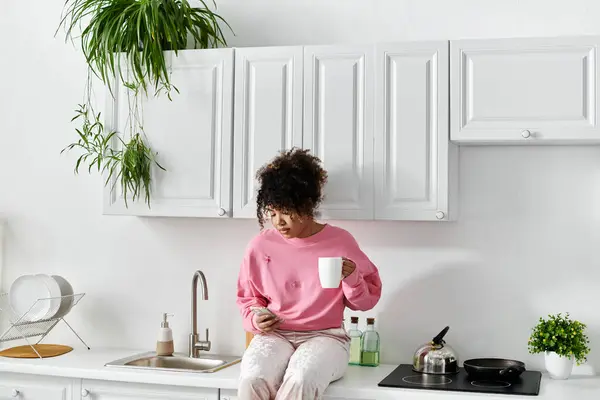 A young woman sips tea while sitting on her kitchen counter. — Stock Photo