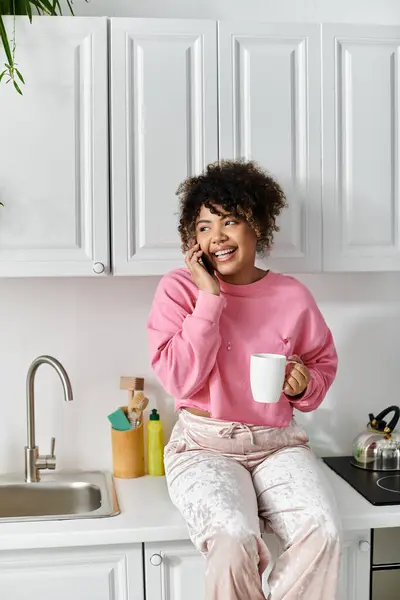 A woman relaxes on her kitchen counter, holding a warm cup while chatting. — Stock Photo