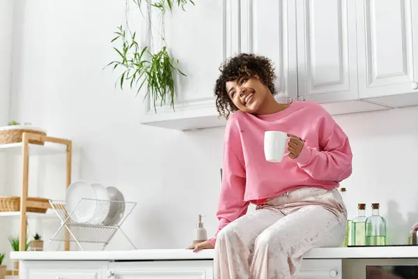 A young woman relaxes at home, sipping a warm drink and smiling joyfully. — Stock Photo