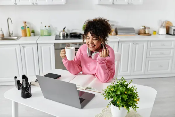 Cheerful woman relaxes with coffee and studies in a bright, modern kitchen. — Stock Photo