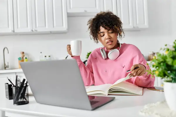 A cheerful woman immersed in study while sipping coffee at her kitchen table. — Stock Photo