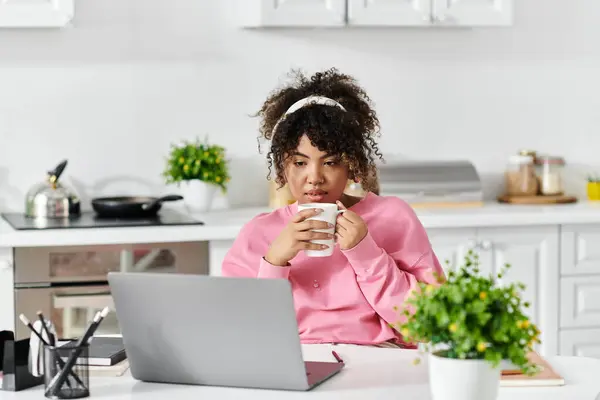 Relaxante em casa, uma mulher bebe café e se concentra em seu laptop. — Fotografia de Stock