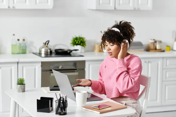 A young woman in a pink sweater focuses on her laptop at home. — Stock Photo