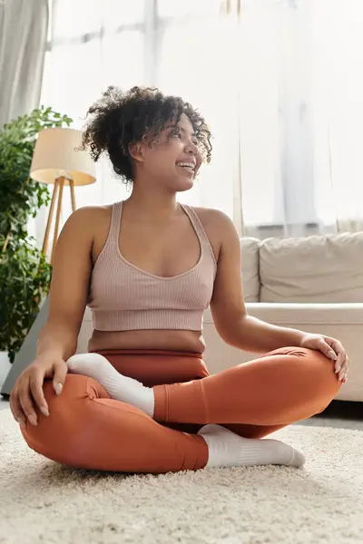 Une jeune femme sourit en s'asseyant les jambes croisées dans son salon. — Stock Photo