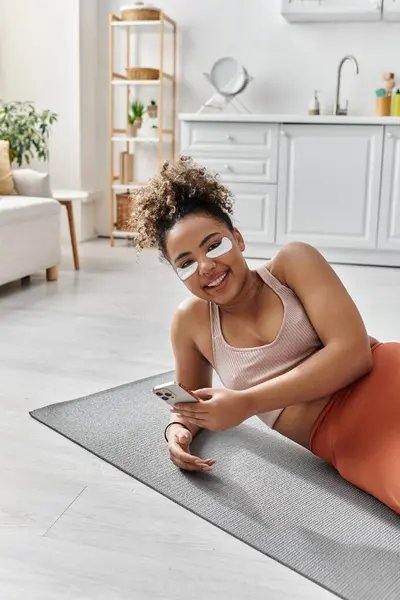 A young woman lounges comfortably at home, smiling while texting. — Stock Photo