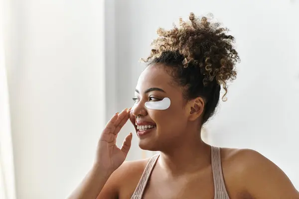 A young woman smiles while relaxing at home, treating herself to some skincare. — Stock Photo