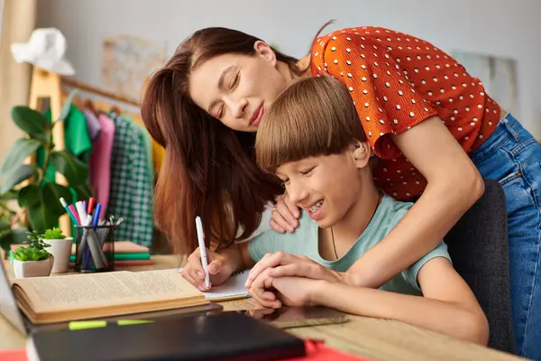 A caring mother supports her son as he learns at a desk. — Stock Photo