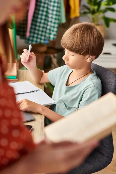 A mother engages with her hearing impaired son while he focuses on his studies. — Stock Photo