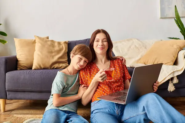 Uma mãe gosta de chá enquanto seu filho abraça perto e observa seu trabalho no laptop. — Fotografia de Stock