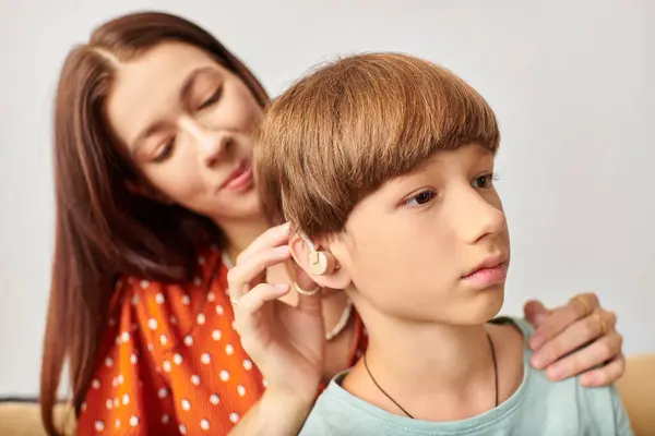 Mãe ajuda seu filho com um aparelho auditivo em um espaço acolhedor. — Fotografia de Stock