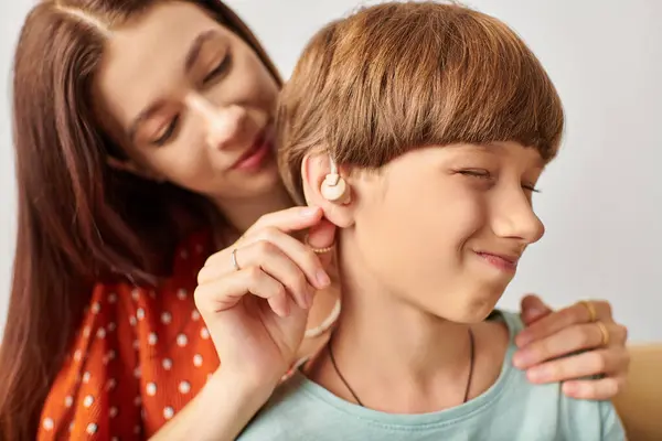 Una madre ayuda amorosamente a su hijo con problemas auditivos con su audífono. — Stock Photo