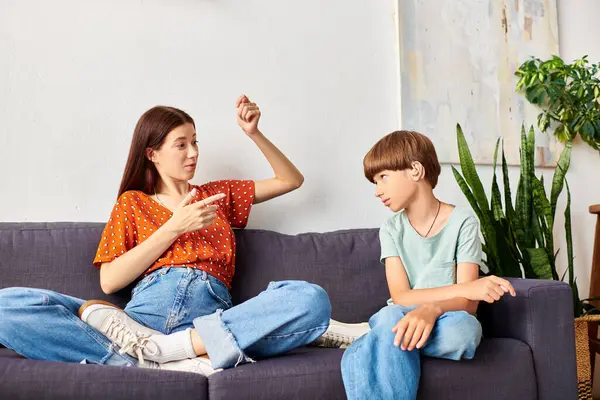 A caring mother interacts warmly with her hearing impaired son on the sofa. — Stock Photo