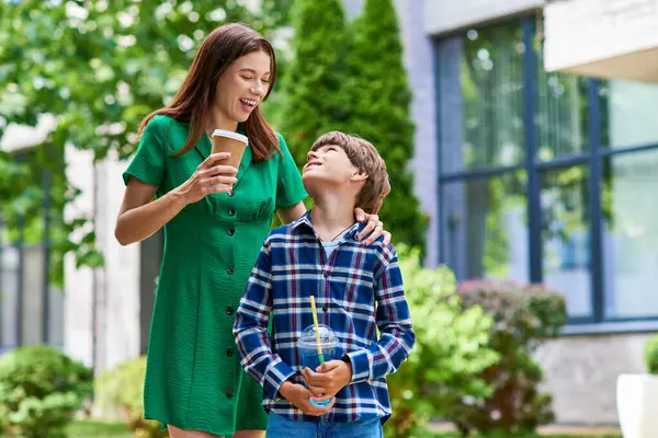 Una madre ríe con su hijo con problemas auditivos mientras disfruta de bebidas al aire libre. — Stock Photo