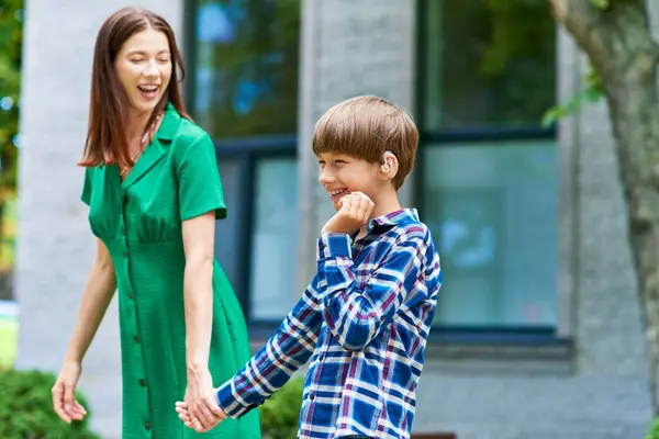 A mother shares a joyful moment with her hearing impaired son in a vibrant park. — Stock Photo