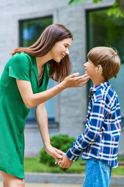 A mother lovingly interacts with her hearing impaired son in a sunny garden. — Stock Photo