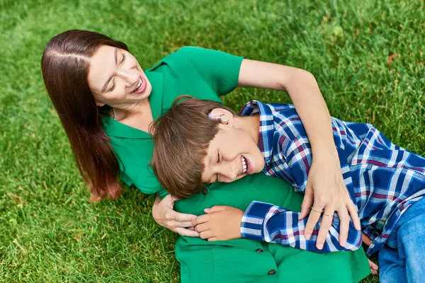 A mother and her hearing impaired son enjoy playful laughter in a vibrant green field. — Stock Photo
