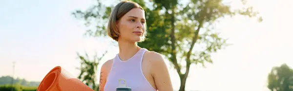 Una bella donna passeggia attraverso un parco, tenendo attrezzature per l'allenamento sotto il sole. — Foto stock