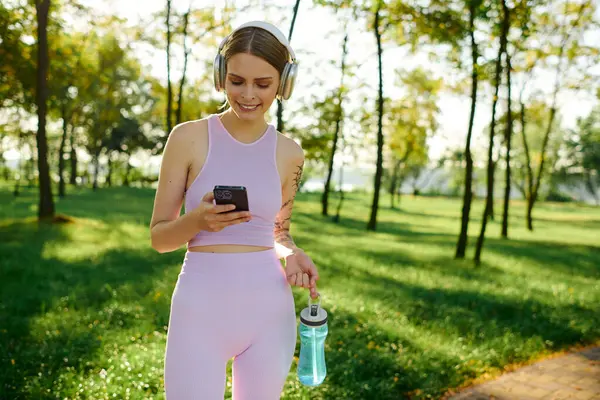 Smiling woman listens to music while checking her phone in a lush park. — Stock Photo