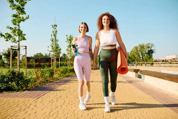Two women walk together, smiling and enjoying their time outdoors in the sunshine. — Stock Photo