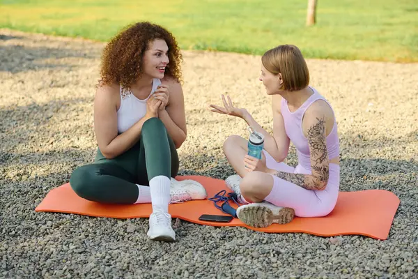 Couple laughs and chats while relaxing on yoga mats in a serene park setting. — Stock Photo