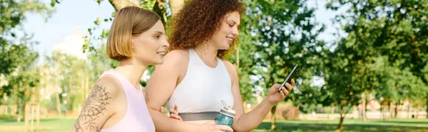 Дві жінки діляться сміхом під час перевірки телефону в парку. — стокове фото