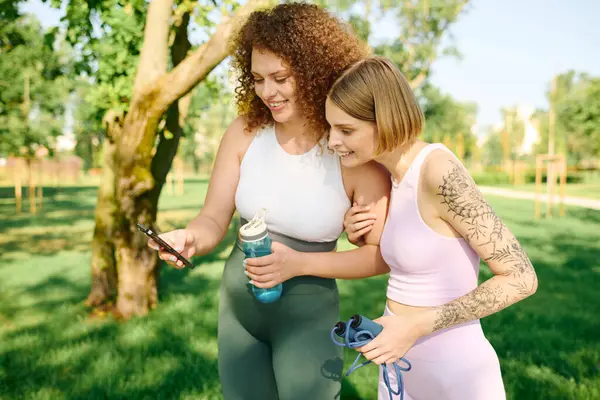 Due donne condividono un momento gioioso mentre controllano il loro telefono all'aperto. — Foto stock