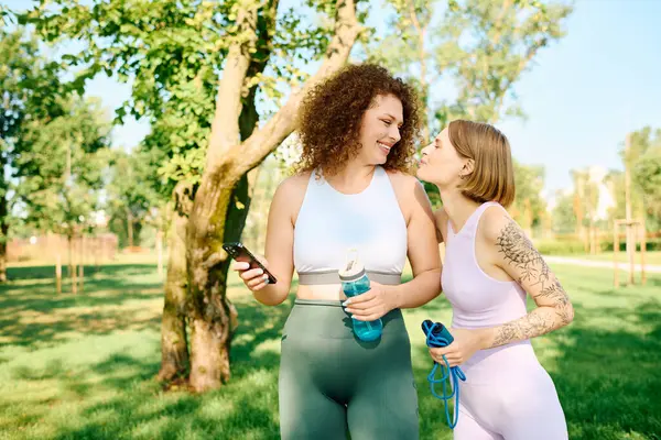 Duas mulheres compartilham riso e carinho em um parque iluminado pelo sol. — Stock Photo