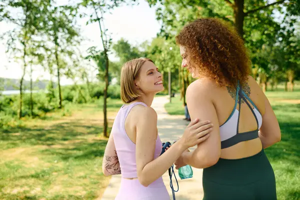 Zwei Frauen teilen Lächeln und Lachen beim Spaziergang durch einen sonnenbeschienenen Park. — Stock Photo