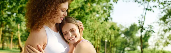 Zwei Frauen umarmen sich herzlich und lächeln in einem üppig grünen Park unter der Sonne. — Stockfoto