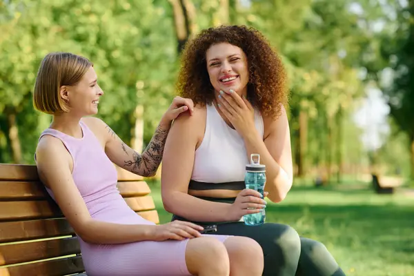 Duas mulheres se divertem enquanto relaxam em um banco no parque. — Fotografia de Stock