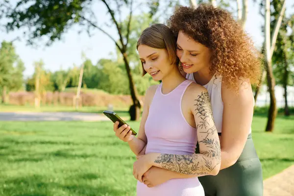 Duas mulheres se deleitam uma com a outra enquanto verificam seu telefone. — Fotografia de Stock