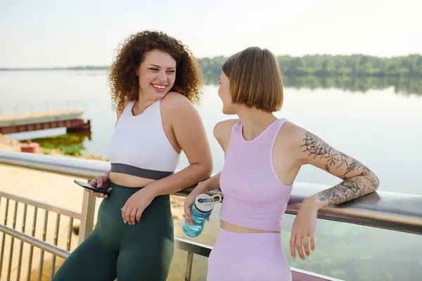 Two women connect and laugh while relaxing near a serene lakeside. — Stock Photo