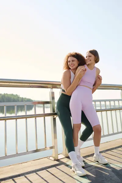 Two women embrace happily on a sunny day by the water. — Stock Photo