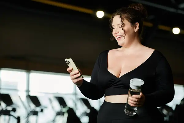 A plus-size woman embraces body positivity, smiling as she interacts with her phone during a workout. — Stock Photo
