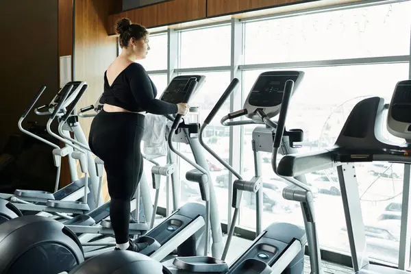 A plus-size woman confidently exercises on an elliptical, celebrating her fitness journey. — Stock Photo