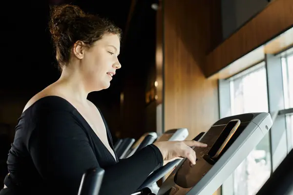 Una joven mujer de talla grande se ejercita con confianza en una elíptica, celebrando su viaje de fitness. — Stock Photo