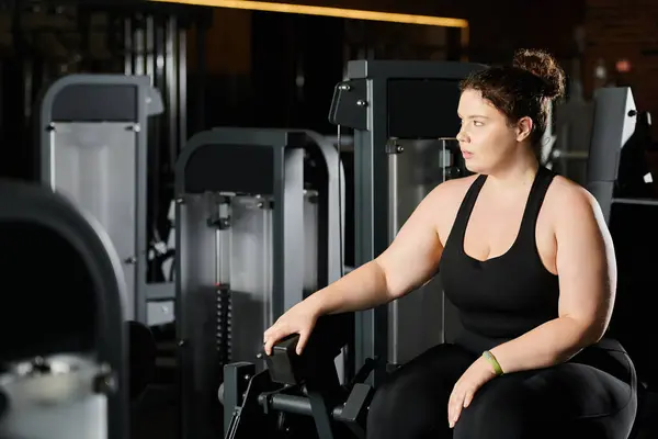 Una mujer de talla grande se centra en su entrenamiento, promoviendo la fuerza y la autoaceptación en un gimnasio enérgico. - foto de stock